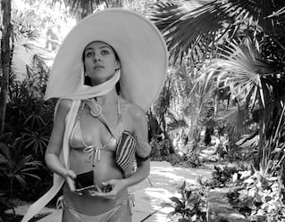 Una mujer en un traje de baño y un gorro de gran tamaño paseando por el sendero de un jardín